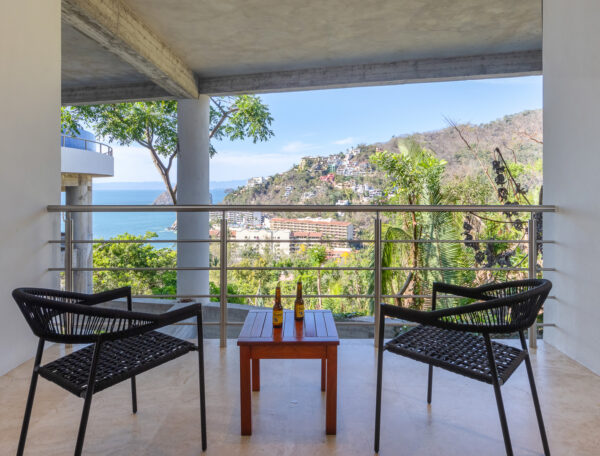 Villa Magnifico Balcony view: two wicker chairs, table with beers, overlooking Mismaloya's greenery, town, and ocean near Puerto Vallarta.