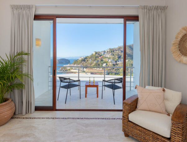 Villa Magnifico Living room with wicker chair and potted plant, leading to ocean-view balcony in Mismaloya, near Puerto Vallarta.