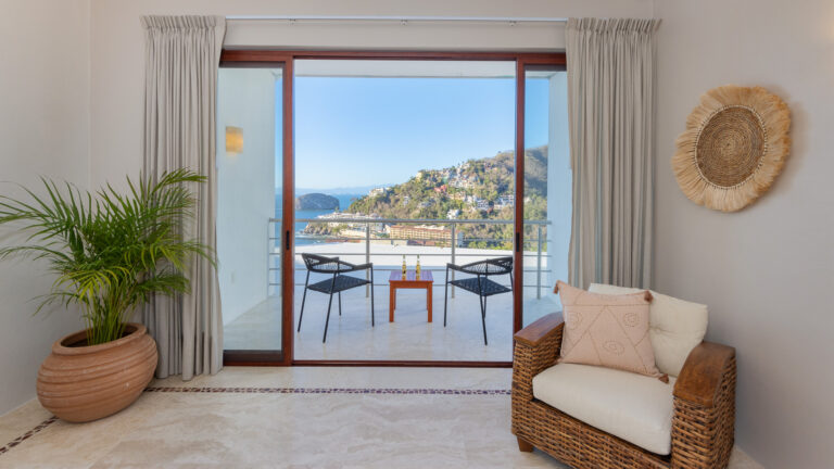 Villa Magnifico Living room with wicker chair and potted plant, leading to ocean-view balcony in Mismaloya, near Puerto Vallarta.