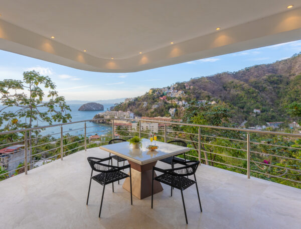 Villa Magnifico Luxury Mismaloya Villa balcony, near Puerto Vallarta, Mexico; dining set overlooks ocean, lush hills, and clear sky.