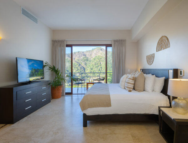 Villa Magnifico Spacious bedroom in luxury villa, Mismaloya, Mexico; features balcony with hill views, plant, TV on dark dresser.