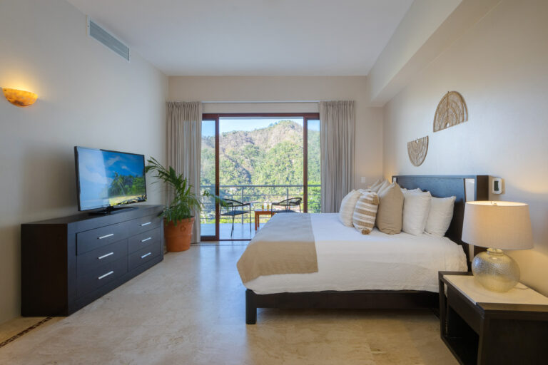 Villa Magnifico Spacious bedroom in luxury villa, Mismaloya, Mexico; features balcony with hill views, plant, TV on dark dresser.
