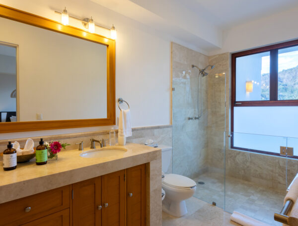 Villa Magnifico Luxury villa bathroom in Mismaloya, near Puerto Vallarta: wooden vanity, large mirror, glass shower, and sunlight-filled window.