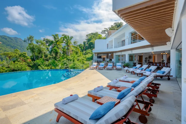 Villa Magnifico Luxury villa in Mismaloya near Puerto Vallarta: white chaise lounges by an infinity pool, modern building, lush trees.