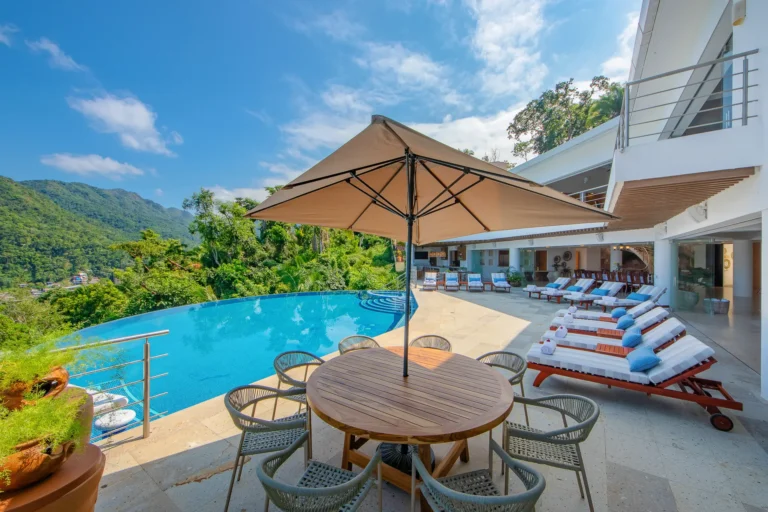 Villa Magnifico Luxurious Villa in Mismaloya, Mexico: outdoor pool, round table with chairs, loungers overlooking lush green hills.