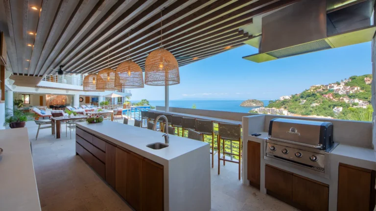 Villa Magnifico Luxury vacation Villa in Mismaloya, Mexico: Modern outdoor kitchen with ocean view, wooden beams, wicker lights, lush hills.