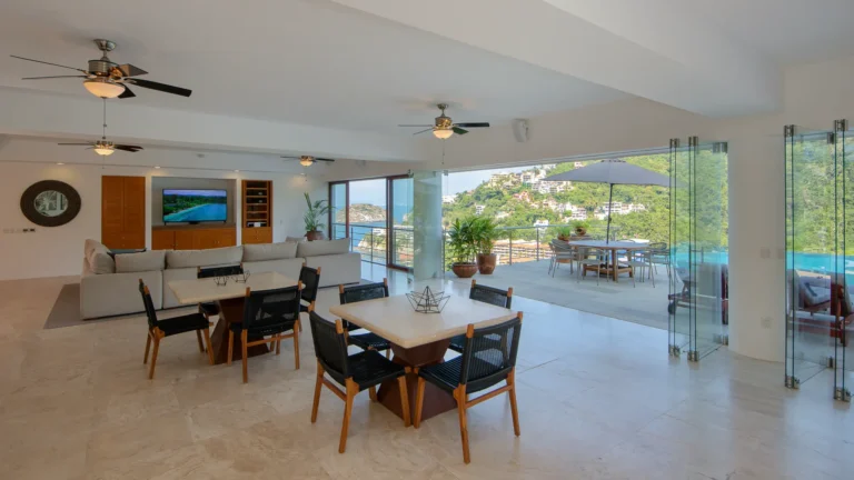 Villa Magnifico Modern living-dining area in a Mismaloya, Puerto Vallarta villa; glass doors open to lush hill views.