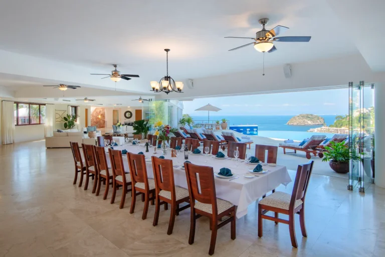 Villa Magnifico Luxurious Villa in Mismaloya, Puerto Vallarta: Elegant dining, open lounge, ocean view through large glass doors with loungers and greenery.