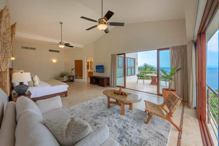 Villa Magnifico Luxury vacation villa in Mismaloya, near Puerto Vallarta: Large airy room, ocean-view balcony, bed, sofa, chairs, serene decor.