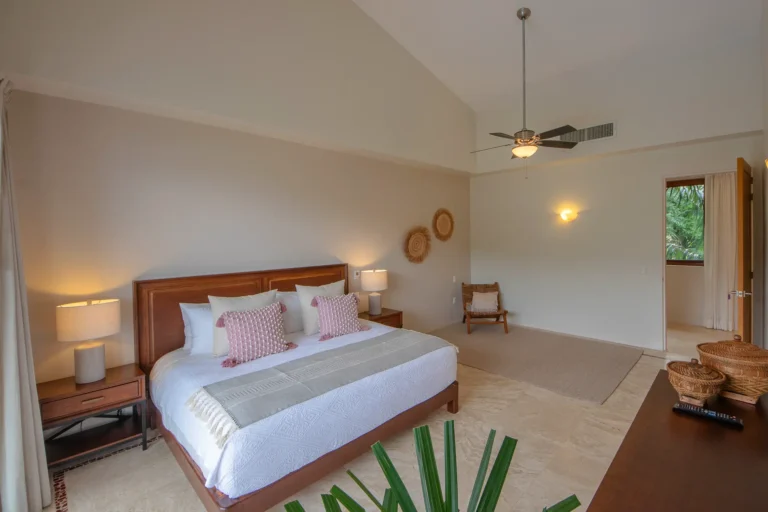 Villa Magnifico Spacious bedroom with white-pink decor, vaulted ceiling, wooden furniture. Open door reveals greenery. Mismaloya, near Puerto Vallarta.
