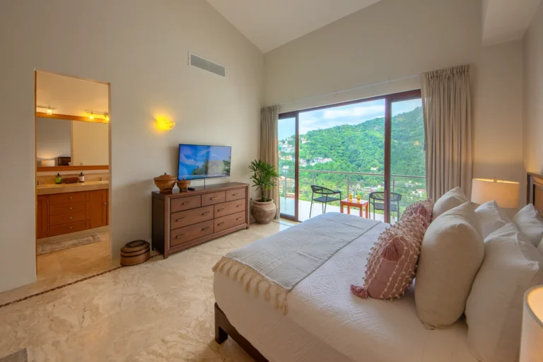 Villa Magnifico Luxury Villa in Mismaloya: Spacious bedroom with balcony views of green hills, open bathroom; cozy cream decor.