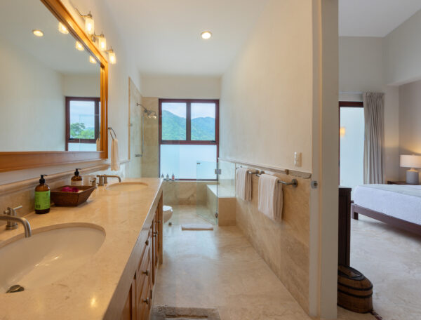 Villa Magnifico Modern bathroom with dual sinks and glass shower; window views green hills in Mismaloya near Puerto Vallarta, Mexico.