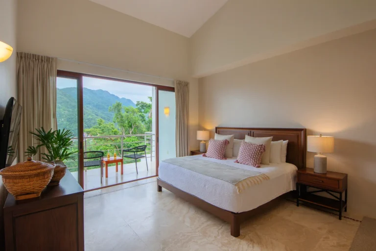 Villa Magnifico A bright bedroom in Mismaloya, near Puerto Vallarta, with a balcony view of green hills and marble flooring.