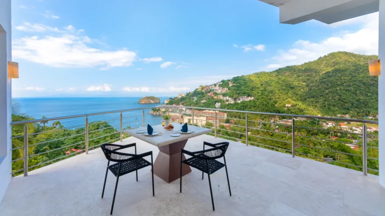 Villa Magnifico Luxury villa balcony in Mismaloya near Puerto Vallarta, Mexico; table, chairs, coastal town, green hills, ocean.