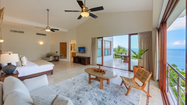 Villa Magnifico Luxurious Villa in Mismaloya: Ocean-view room with king bed, TV, seating area, and balcony amid greenery near Puerto Vallarta.