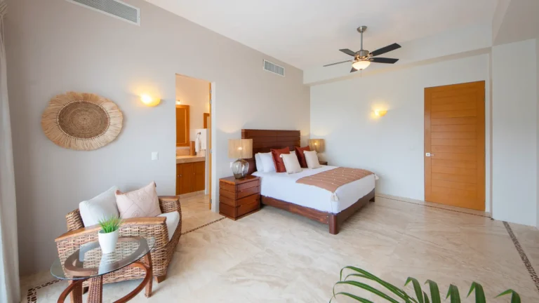 Villa Magnifico Hotel room in Mismaloya, near Puerto Vallarta: Queen bed, wooden nightstands, wicker chair, tiled floors, neutral walls.