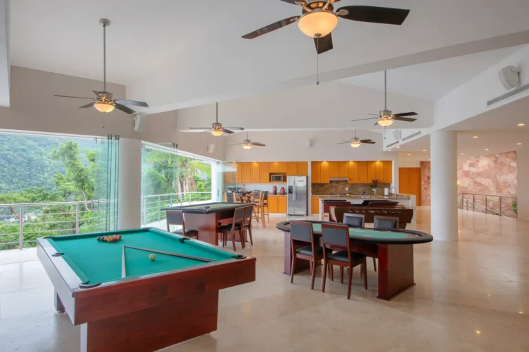 Villa Magnifico Open recreation room with pool and card tables, kitchenette; large windows show lush greenery. Mismaloya, near Puerto Vallarta.