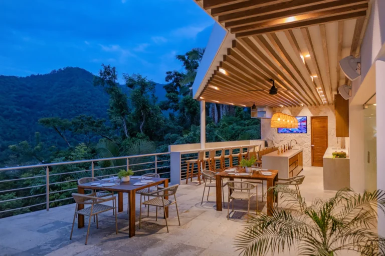 Villa Magnifico Dusk view of Mismaloya, near Puerto Vallarta: patio with dining table, bar, lights; overlooks forested hills.