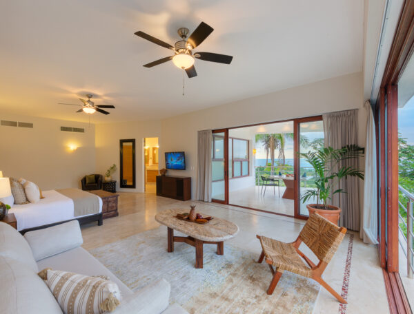 Villa Magnifico Luxury Villa bedroom in Mismaloya, Mexico: neutral tones, large bed, sitting area, flat-screen TV, ocean-view windows.