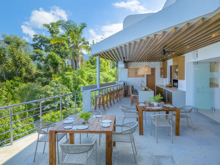 Villa Magnifico Outdoor dining with wooden tables and bar under canopy, surrounded by greenery, in Mismaloya near Puerto Vallarta.