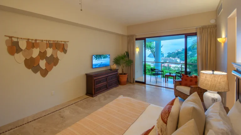 Villa Magnifico Living room overlooking lush Mismaloya landscape, near Puerto Vallarta: TV, plant, beige sofa with patterned cushions.