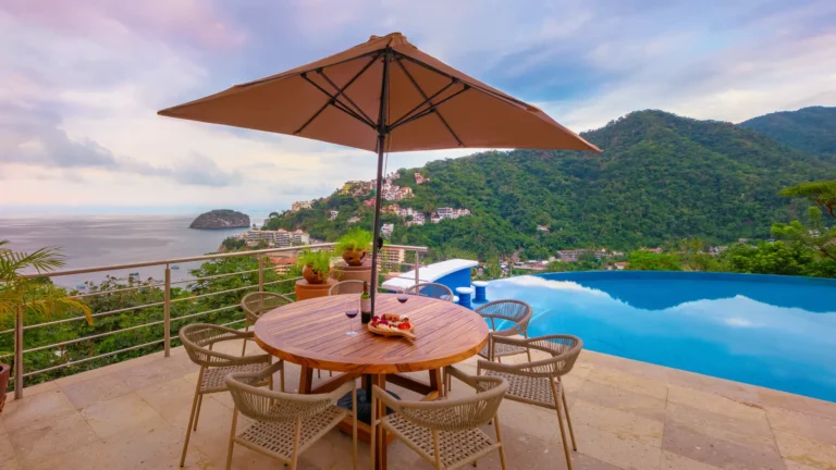 Villa Magnifico Luxury villa in Mismaloya: Table under umbrella beside infinity pool, overlooking lush hills and bay near Puerto Vallarta.
