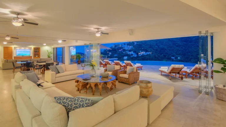 Villa Magnifico Open-plan living room with terrace overlooking Mismaloya’s mountains near Puerto Vallarta, Mexico; glass doors connect spaces.