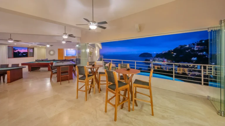 Villa Magnifico Spacious villa room in Mismaloya, Mexico: tile floors, ceiling fans, game tables; balcony view of hills and city lights.