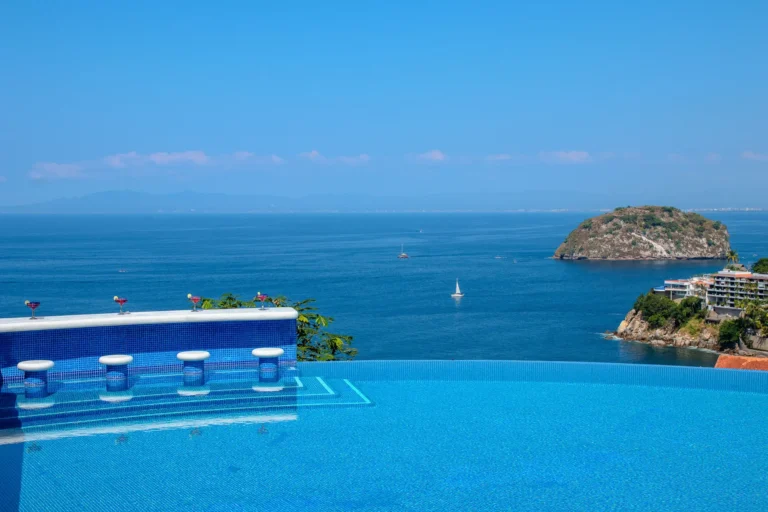 Villa Magnifico Infinity pool at a luxury Mismaloya villa, with ocean view near Puerto Vallarta, Mexico; sailboat by lush island.