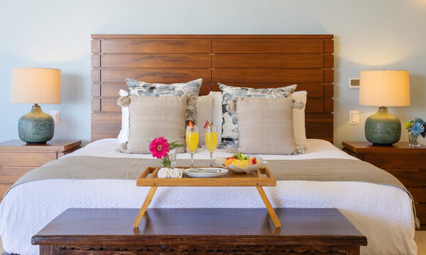 Villa Magnifico Luxurious Mismaloya villa bedroom near Puerto Vallarta: wooden headboard, bedside lamps, tray with juices, flower arrangement.