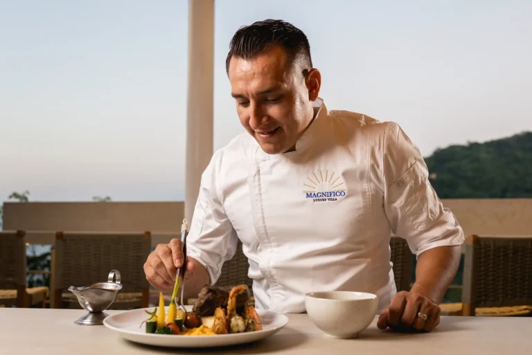 Villa Magnifico A chef in white garnishes a dish with vegetables and meat outdoors in Mismaloya, near Puerto Vallarta, Mexico.