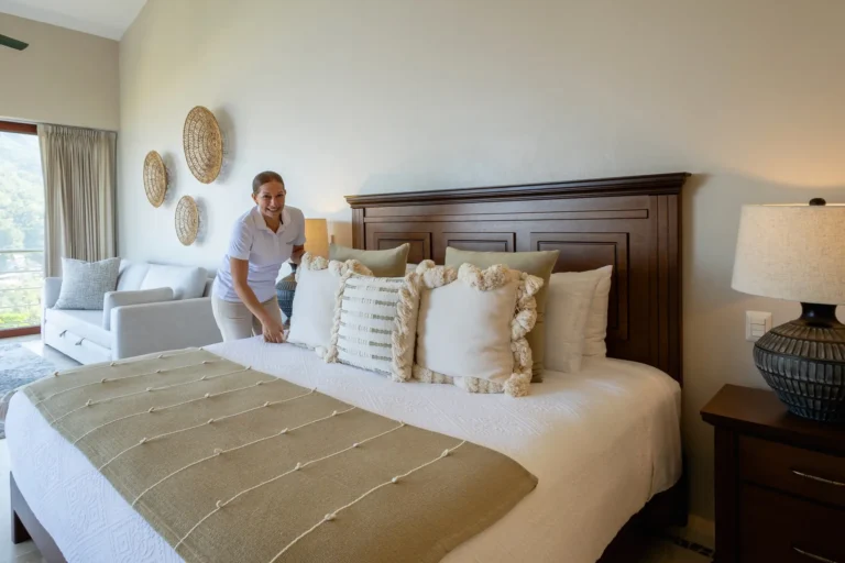 Villa Magnifico A person in white uniform makes a bed with pillows and throw in a Mismaloya luxury villa bedroom.