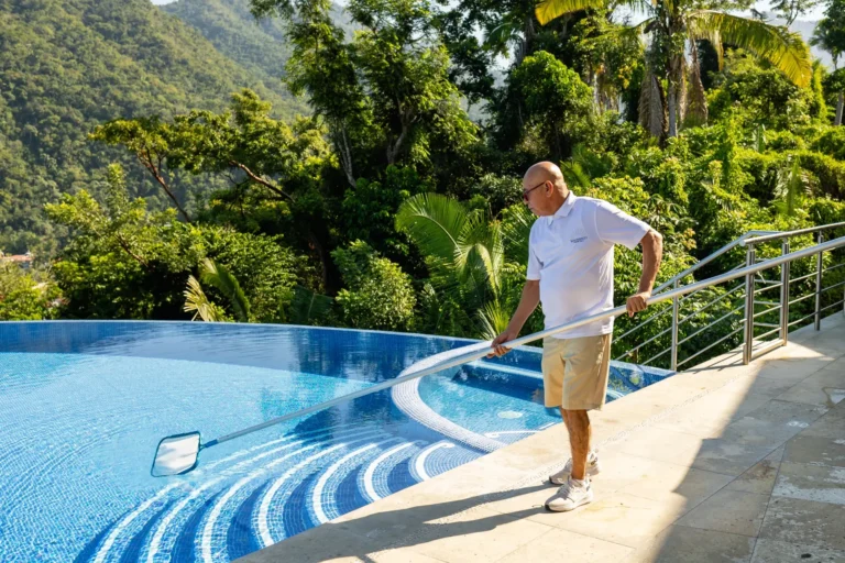 Villa Magnifico A person cleans an infinity pool at a luxury villa in Mismaloya, near Puerto Vallarta, surrounded by lush hills.