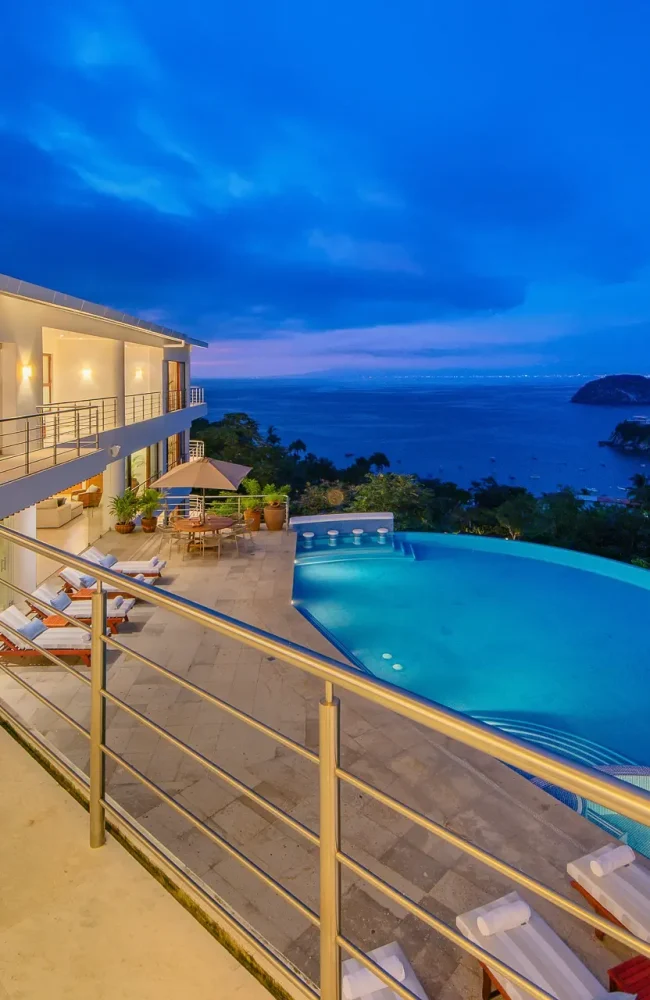 Villa Magnifico Mismaloya, near Puerto Vallarta: Balcony with infinity pool merging into ocean view; loungers and umbrellas on patio.